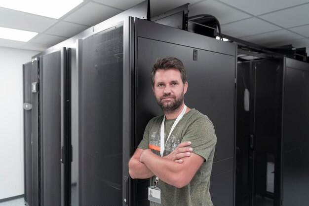 Portrait of male technician or network administrator standing brave as a hero with arms crossed in data center server room. High quality photo