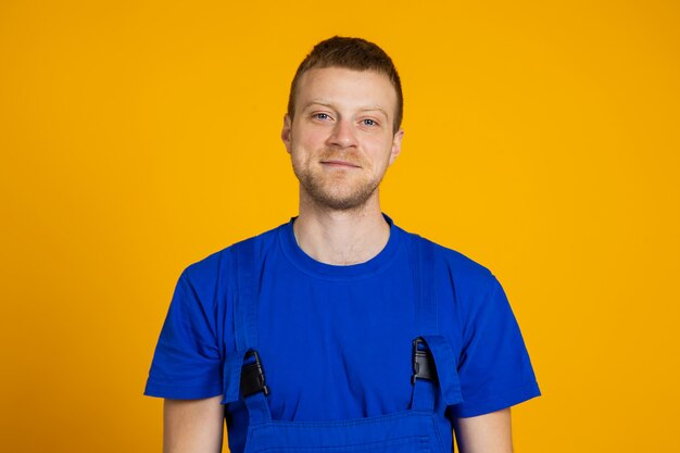 Portrait of a male worker in overalls. red-haired young technician on a yellow background