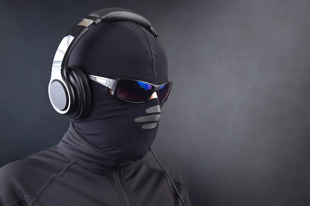 Portrait of a man in a black mask and sunglasses listening to music on headphones