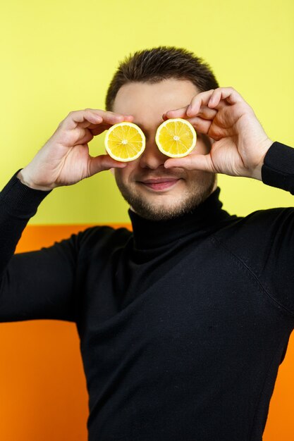 Portrait of a man in black raglan with cut lemon instead of eyes. A guy with lemons near his face. A smile on his face