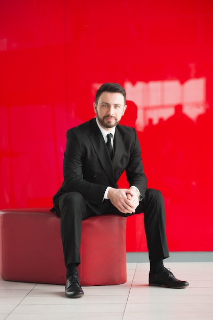 Portrait of man in black suit sits on red seat