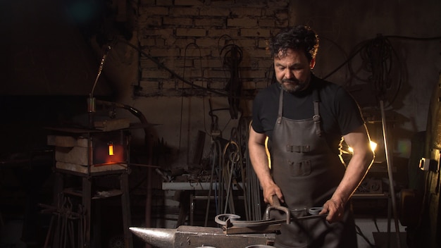 Portrait of a man of a blacksmith in the working atmosphere. Brutal man looks and smiles.