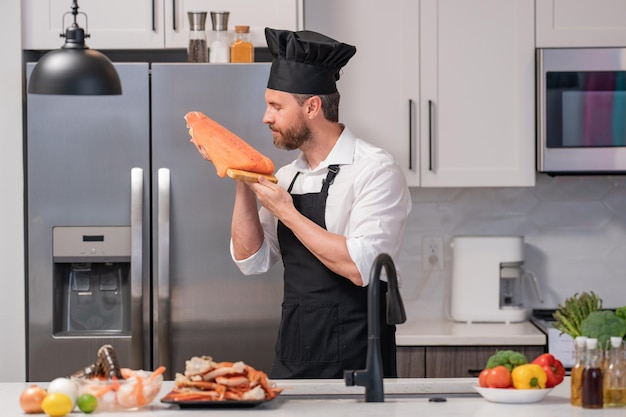 Portrait of man in chef apron and cook hat preparing fresh natural meal salmon at kitchen handsome c