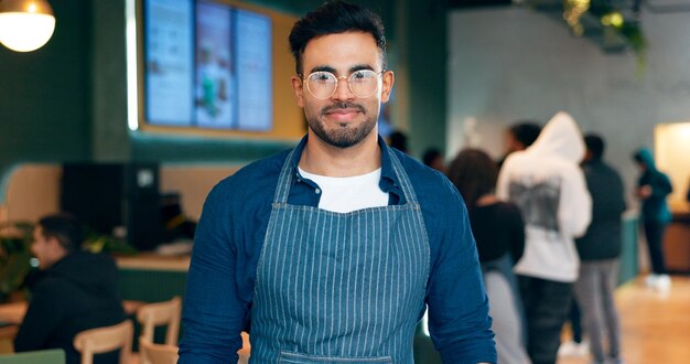 Portrait man or employee with smile in coffee shop for small business management or work Male waiter glasses and confidence in apron by entrance for welcome customer and restaurant for service