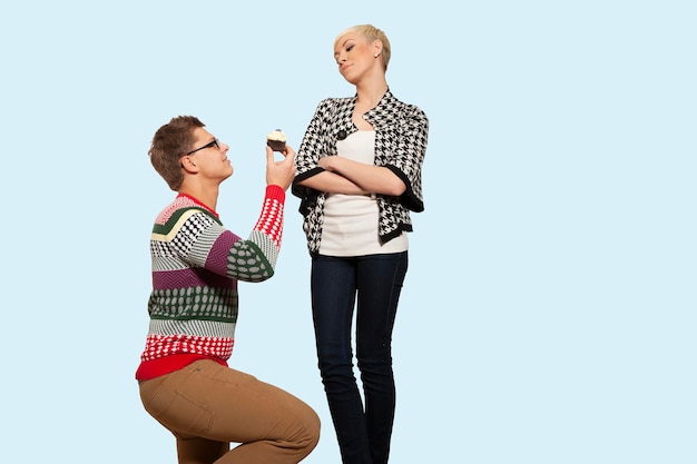 Portrait of a man and a girl proposing to her with a delicious pastry or cake on a light blue pastel isolated background. Cute attractive funny funny positive crazy. Close-up.