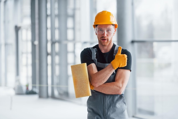 Portrait of man in grey uniform that standing indoors in modern big office at daytime with equipment in hand