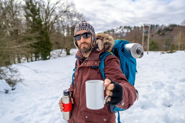 Portrait of man having breakfast a hot coffee from a thermos in winter in the snow