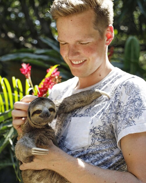 Photo portrait of man holding baby sloth outdoors