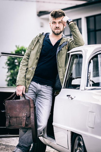 portrait of man holding briefcase while leaning on car