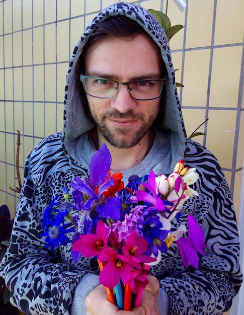 Photo portrait of man holding colorful flowers against wall