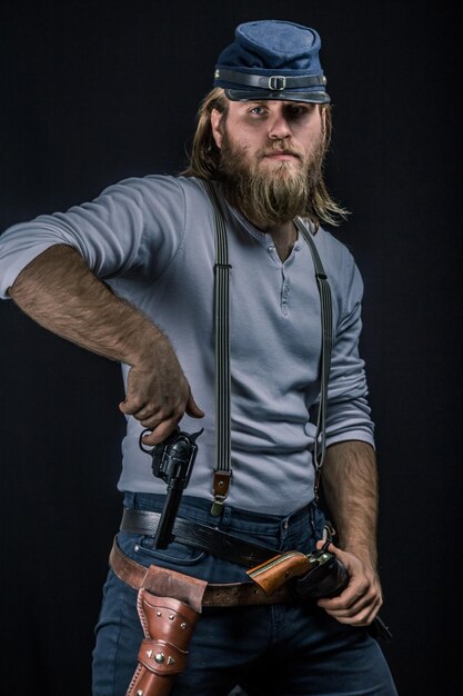 Portrait of man holding gun while standing against black background