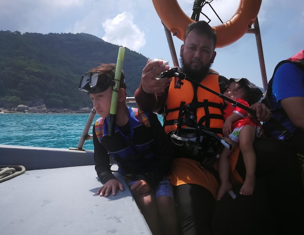 Photo portrait of man holding monopod while sitting with children in boat