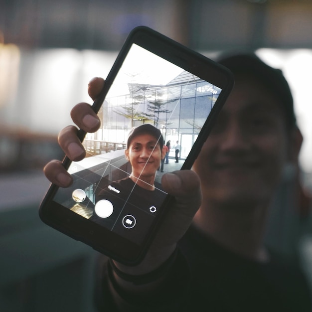 Photo portrait of man holding smart phone seen on device screen outdoors