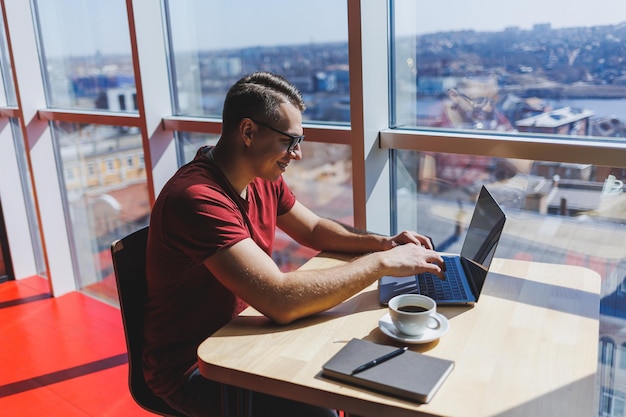 Portrait of a man it professional working remotely with a\
modern laptop sitting at a table and smiling at the camera during a\
break a happy human programmer in vision correction glasses