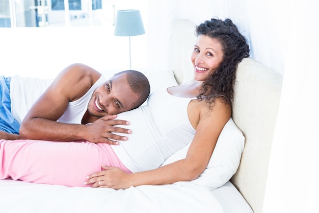 Portrait of man listening to belly of pregnant wife on bed