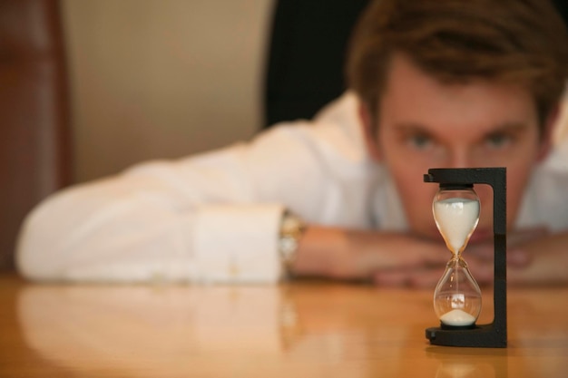 Photo portrait of man looking at hourglass on table