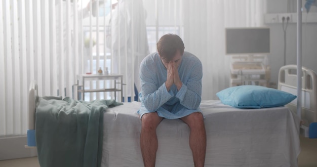 Portrait of man patient sitting on bed in hospital feeling stressed