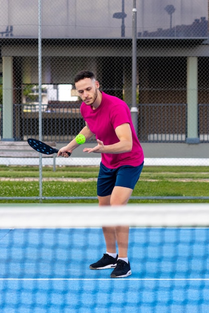 피클볼에서 서브를 수행하는 남자의 초상화 스포티한 남자 피클볼 테니스 선수가 라켓을 사용하여 공을 치는 야외 코트에서 훈련합니다.