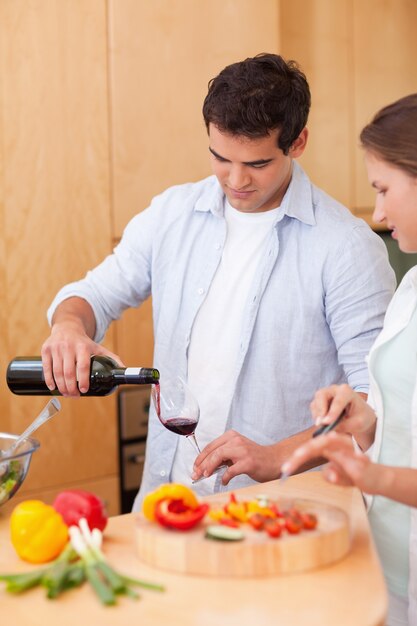 Portrait of a man pouring a glass of wine while his wife is cooking