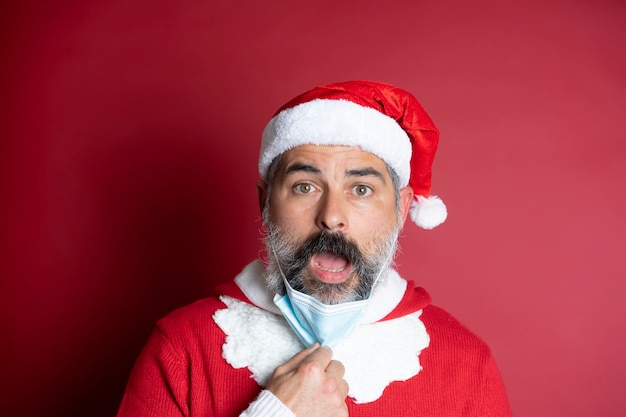 Portrait of man in Santa hat takes off medical facial mask from his face