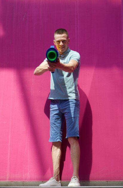 Portrait of man shooting with toy handgun while standing against pink wall