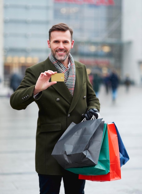 Foto ritratto di un uomo che mostra una carta di credito mentre tiene delle borse della spesa in città durante l'inverno