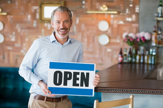 Portrait of man showing signboard with open sign