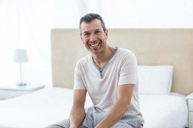 Portrait of man sitting on bed and smiling in bedroom