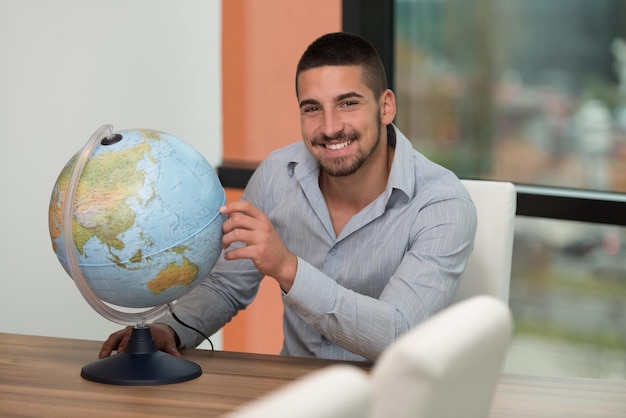 Portrait Of A Man Sitting By His Desk And Holding A Globe Model