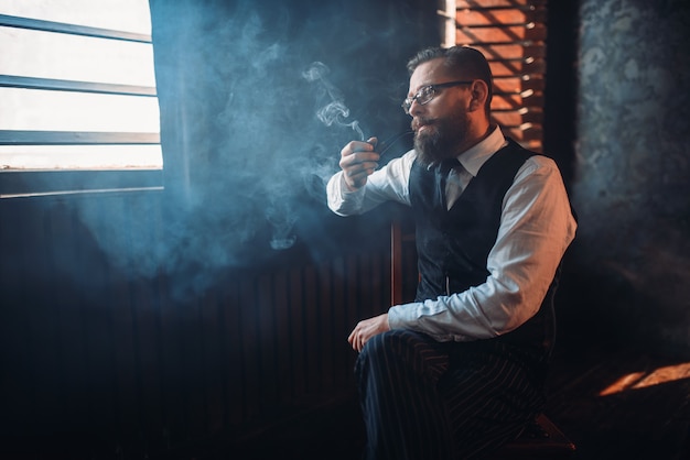 Portrait of man sitting on chair and smoking pipe