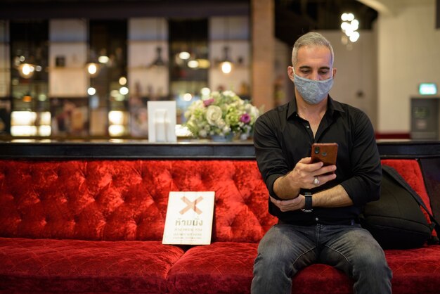 Portrait of man sitting while social distancing and using mobile phone