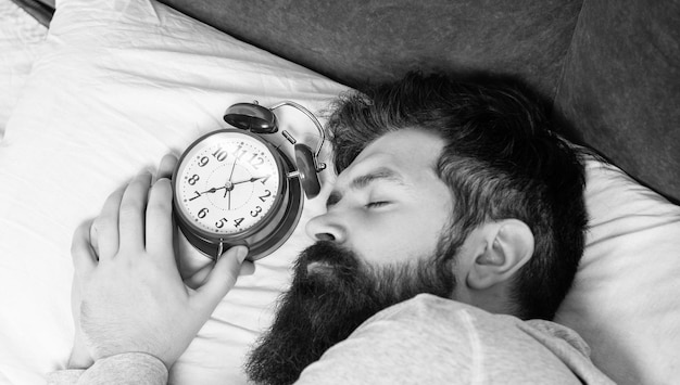 ベッドの睡眠時間に目覚まし時計で寝ている男の肖像