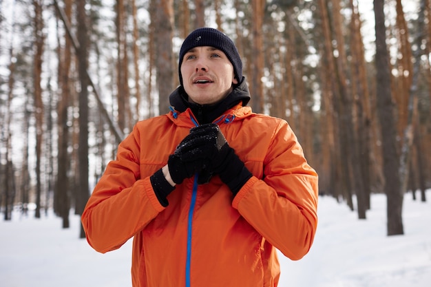 Ritratto di un uomo che si estende nel parco in una bella giornata invernale innevata, preparandosi per la corsa