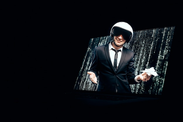 Portrait of a man in a suit and helmet. He launches a paper airplane from a laptop screen. 