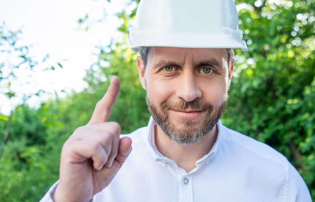 Portrait of man supervisor in hardhat pointing finger up outdoors