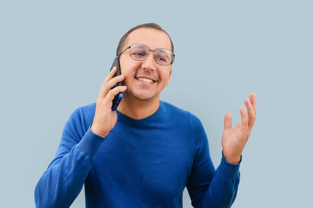 Photo portrait of a man in a sweater with a smartphone in his hands on a blue background