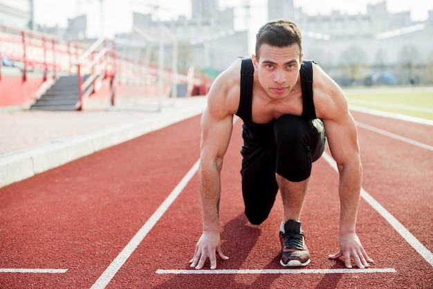 Foto ritratto di un uomo che prende la posizione per correre sulla pista di atletica