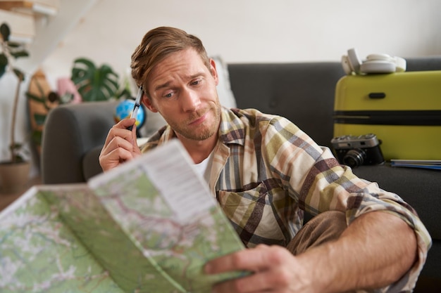 Photo portrait of man tourist looking confused at travel map shrugging cant decide on route choosing the