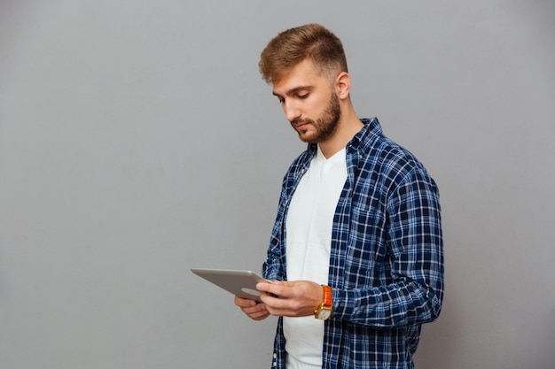 Ritratto di un uomo che utilizza un computer tablet isolato su un muro grigio