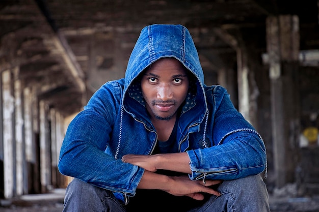 Photo portrait of man wearing denim hooded shirt while sitting in abandoned building