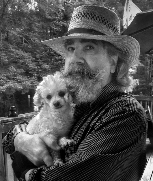 Photo portrait of man wearing hat carrying dog against tree