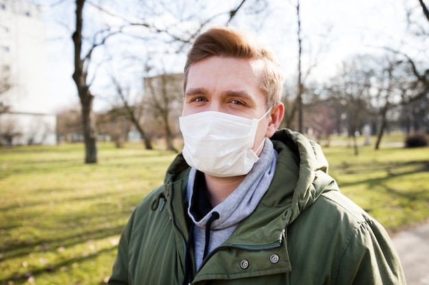 Portrait of a man wearing medical mask on a city public park bacground. Corona virus pandemic. Concept Of Air pollution, Pneumonia Outbreak, smog or Epidemic