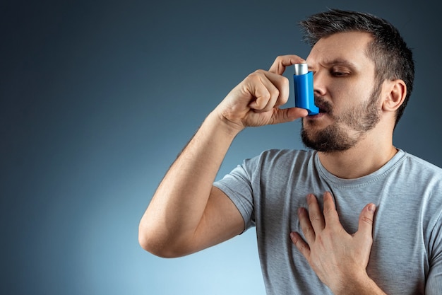 Portrait of a man with an asthma inhaler in his hands, an asthmatic attack. The concept of treatment of bronchial asthma, cough, allergies, dyspnea.