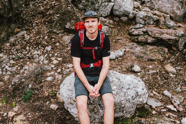 Foto ritratto di un uomo con uno zaino seduto su una roccia