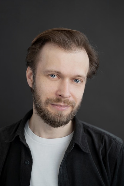 portrait of a man with a beard in a white Tshirt and black shirt on a dark background looks