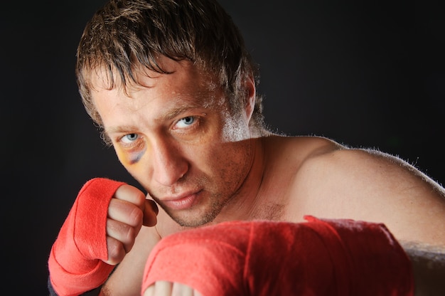 Portrait of a man with a black eye in a battle position. Clenched fists. Dark background.