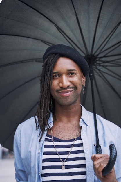 Portrait of a man with dreadlocks and moustache looking at the camera with an umbrella protecting himself from the rain