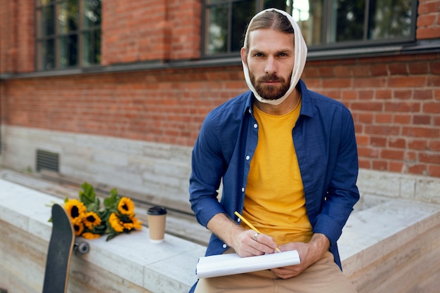 Photo portrait of man with ear bandage sketching on notepad outdoors