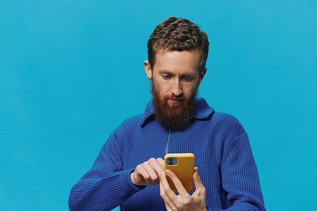 手に電話を持つ男性のポートレートは、青い背景にそれを見て電話で話していますオンラインソーシャルメディアライフスタイルのコミュニケーション