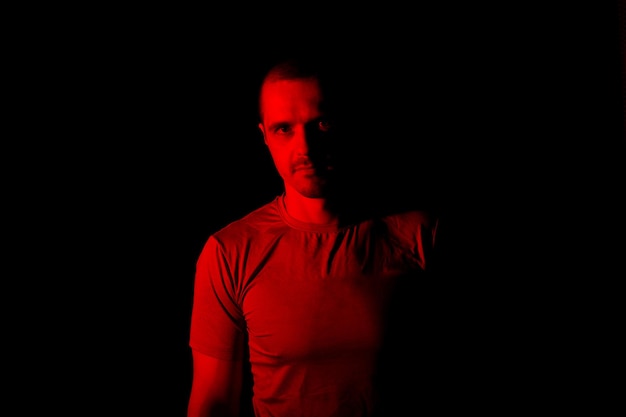 Portrait of man with red light looking in camera standing in studio at black background